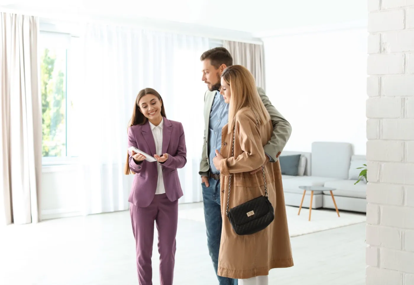 An agent showing a couple through a bright modern apartment