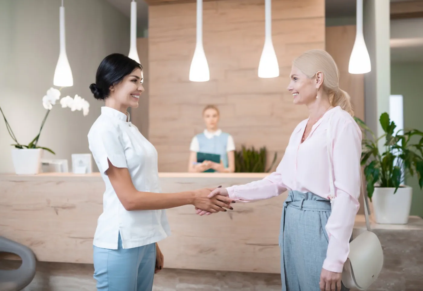 A practitioner greeting a client at a bright clinic reception desk